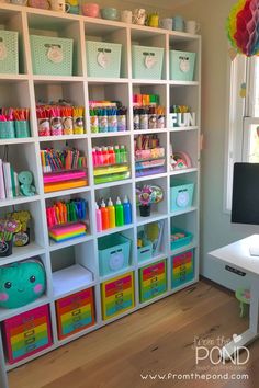 a white bookcase filled with lots of colorful items next to a desk and window