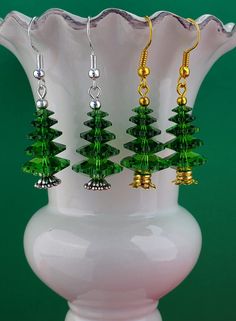 green and gold christmas tree earrings on a white vase in front of a green background