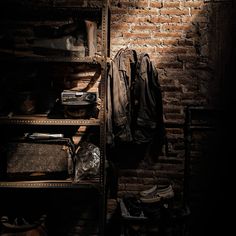 an old closet with clothes and shoes on shelves next to a brick wall in the dark