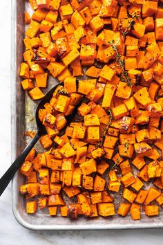 a pan filled with cooked sweet potatoes on top of a white countertop next to a black spoon