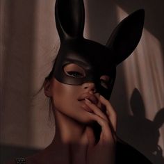 a woman wearing a black bunny mask with her hand on her face and looking at the camera