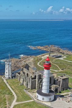 an aerial view of a lighthouse on the coast with blue water in the back ground