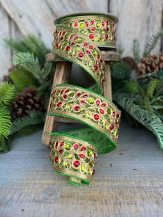 three pieces of green and red beaded ribbon with pine cones in the back ground