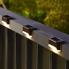 three lights that are on the side of a metal fence with trees in the background