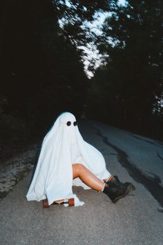 a woman dressed as a ghost sitting on the side of a road with her legs crossed