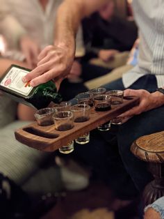 a man is pouring shots into glasses on a tray while others sit in the background