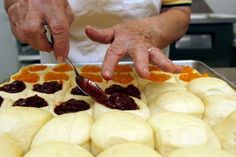 an older person cutting food on top of a pan filled with buns and jelly