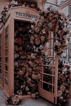 a phone booth covered in fake flowers next to a window with a telephone on it