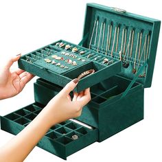 a woman is holding an open green jewelry box with many necklaces and rings in it