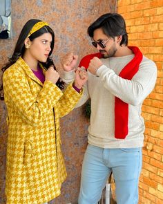 two people standing next to each other in front of a brick wall and one person wearing sunglasses