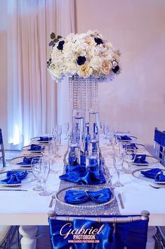 the table is set with blue and white flowers in a tall crystal vase on top of it