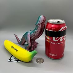 a can of coca - cola next to a small toy lizard and a plastic banana