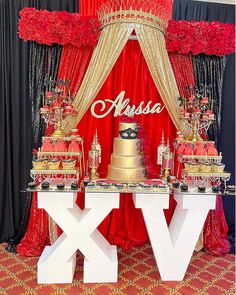 a table topped with lots of cakes and desserts next to a red curtained wall