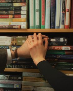 a person reaching for a book in front of a bookshelf full of books