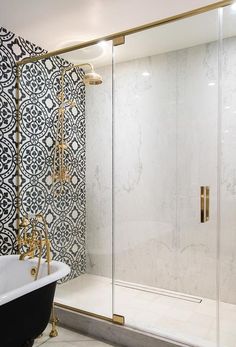 a bath tub sitting next to a shower with a glass door and gold trimming