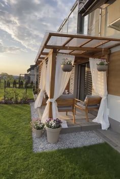 an outdoor patio with curtains and potted plants on the ground next to a house