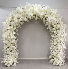 white flowers are arranged in an arch on the floor