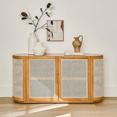 a white vase sitting on top of a wooden sideboard next to a plant and pictures