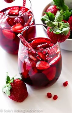 two glasses filled with liquid and strawberries next to each other on a white surface