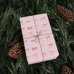 a wrapped present sitting on top of a christmas tree next to pine cones and twine