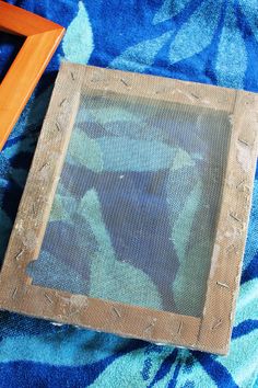 a wooden frame sitting on top of a blue blanket next to a framed photo and an empty piece of wood