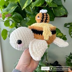 a hand holding a small crocheted stuffed animal next to a potted plant