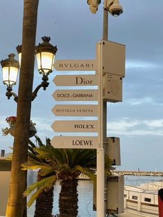 a pole with several signs attached to it next to a body of water and palm trees