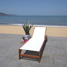 an empty chaise lounge on the beach next to the ocean with a potted plant