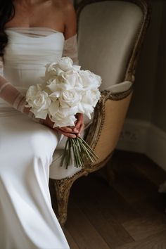 a woman sitting in a chair holding a bouquet of flowers and wearing a white dress