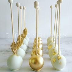 some white and gold cake pops are lined up on a marble counter top with golden leaf decorations