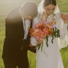 a bride and groom standing in front of a lush green field with flowers on their wedding day