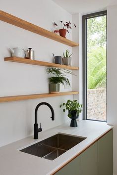 a kitchen sink sitting under a window next to a wooden shelf filled with potted plants