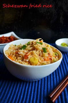 two bowls filled with rice and vegetables next to chopsticks on a blue mat