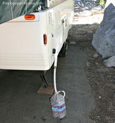 a white camper parked next to a pile of rocks with a water bottle hooked up to it