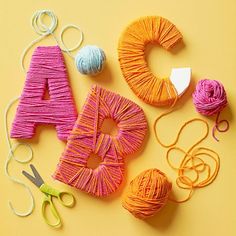 yarn, scissors and balls of thread laid out on a yellow surface with the letter a