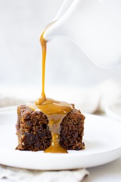 a piece of cake with caramel sauce being drizzled over it on a white plate