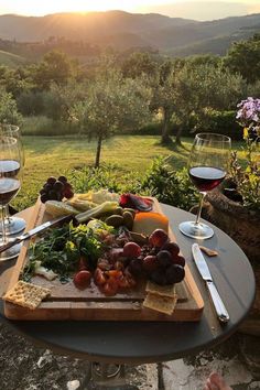 an outdoor table with wine glasses, cheese and fruit on it in front of the sun