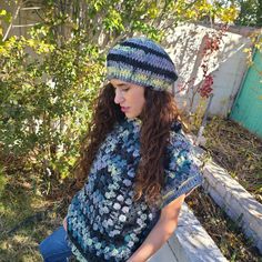 a woman sitting on a bench wearing a knitted ponchy with flowers and leaves