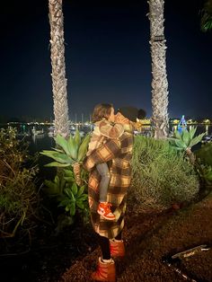 two people standing next to each other in front of palm trees and water at night