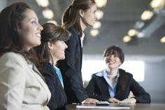 three women in business attire sitting at a table and one woman is holding a cell phone