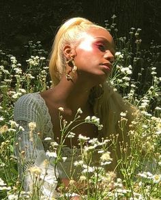 a woman with blonde hair sitting in a field of flowers