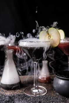 an apple sitting on top of a glass filled with liquid next to other glasses and bottles