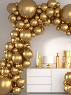 an arch made out of gold balloons in the middle of a room with a white dresser