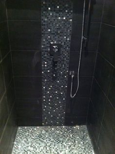 a walk in shower sitting next to a black tiled wall and floor covered in silver mosaic tiles