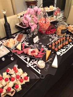 a black table topped with lots of food and desserts next to a bottle of wine