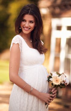 a pregnant woman holding a bouquet of flowers in her hand and smiling at the camera