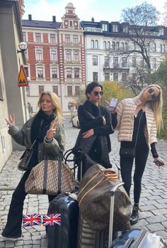 three people are standing around with luggage and one is pointing at something in the air