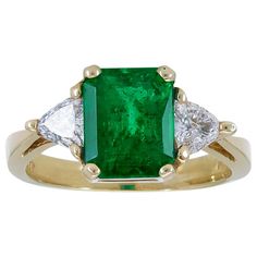 A classic three-stone engagement ring showcasing a color-rich emerald cut green emerald, accented with brilliant trillion (triangular) diamonds on either side. Set in a tapered 18k yellow gold mounting. Emerald weighs 2.59 carats. Diamonds weigh 0.49 carats total. Size 7.5 US (sizable) Dimensions: 0.38 in x 0.68 in. Luxury Gia Certified Trillion Cut Emerald Ring, Luxury Gia-certified Trillion Cut Emerald Ring, Luxury Trillion Cut Emerald Ring For Formal Occasions, Luxury Trillion-cut Emerald Ring, Gia Certified Trillion Cut Emerald Wedding Ring, Green Trillion Cut Diamond Ring, Green Emerald Ring With Three Stone Baguette Cut, Gia Certified Trillion Cut Emerald Rings, Three-stone Emerald Cut Green Emerald Ring