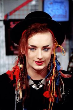 a woman with long red hair wearing a black hat and colorful necklaces on her neck