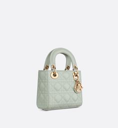 The Lady Dior bag epitomizes the House's vision of elegance and beauty. Sleek and refined, the style is timeless. It is crafted in pistachio green lambskin with Cannage stitching, creating the unmistakable quilted texture. The pale gold-finish metal D.I.O.R. charms embellish and illuminate its silhouette. Featuring a removable chain shoulder strap, the miniature Lady Dior bag can be carried by hand or worn crossbody as an ideal evening wear companion.. Mini Lady Dior, Lady D, Micro Bag, Christian Dior Fashion, Christian Dior Couture, Dior Couture, Balenciaga Designer, Boutique Online, The Lady